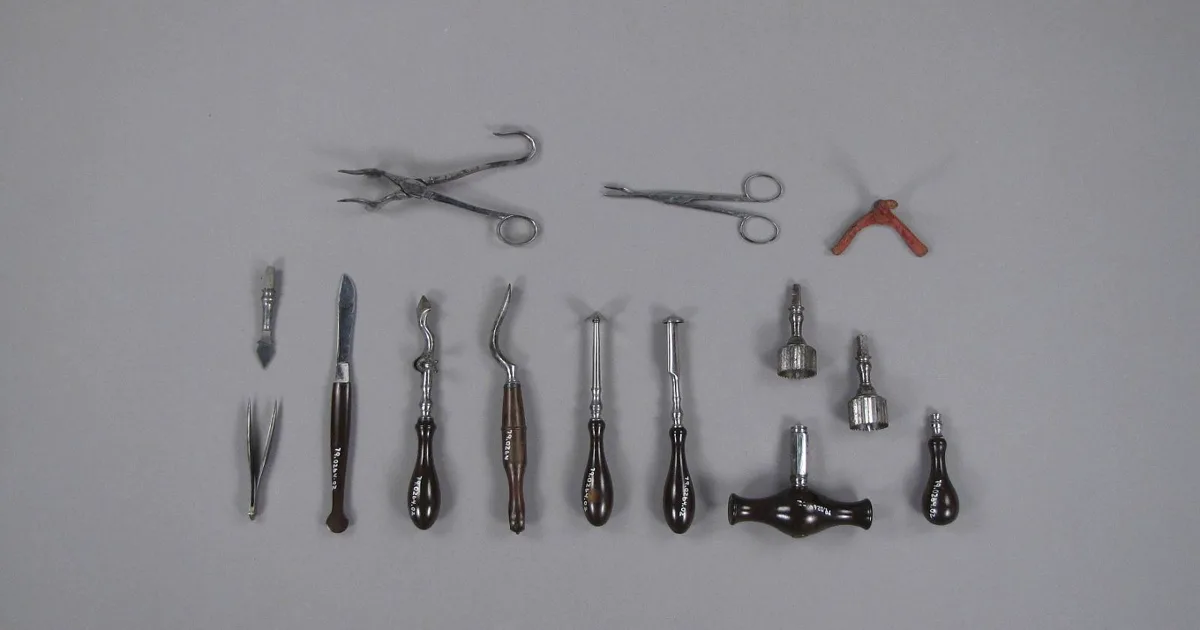 Estuche quirúrgico del siglo XIX extendido sobre fondo gris: pinzas, bisturíes, elevadores y trépanos, cada instrumento con mango de ébano torneado